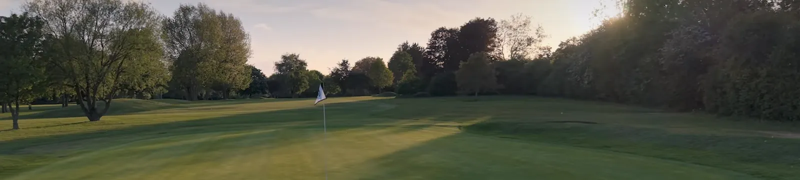 A green with the flag in, in low evening sun.
