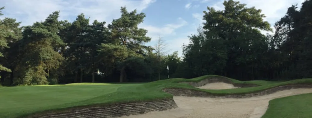 A green guarded by a revetted bunker, with trees behind.